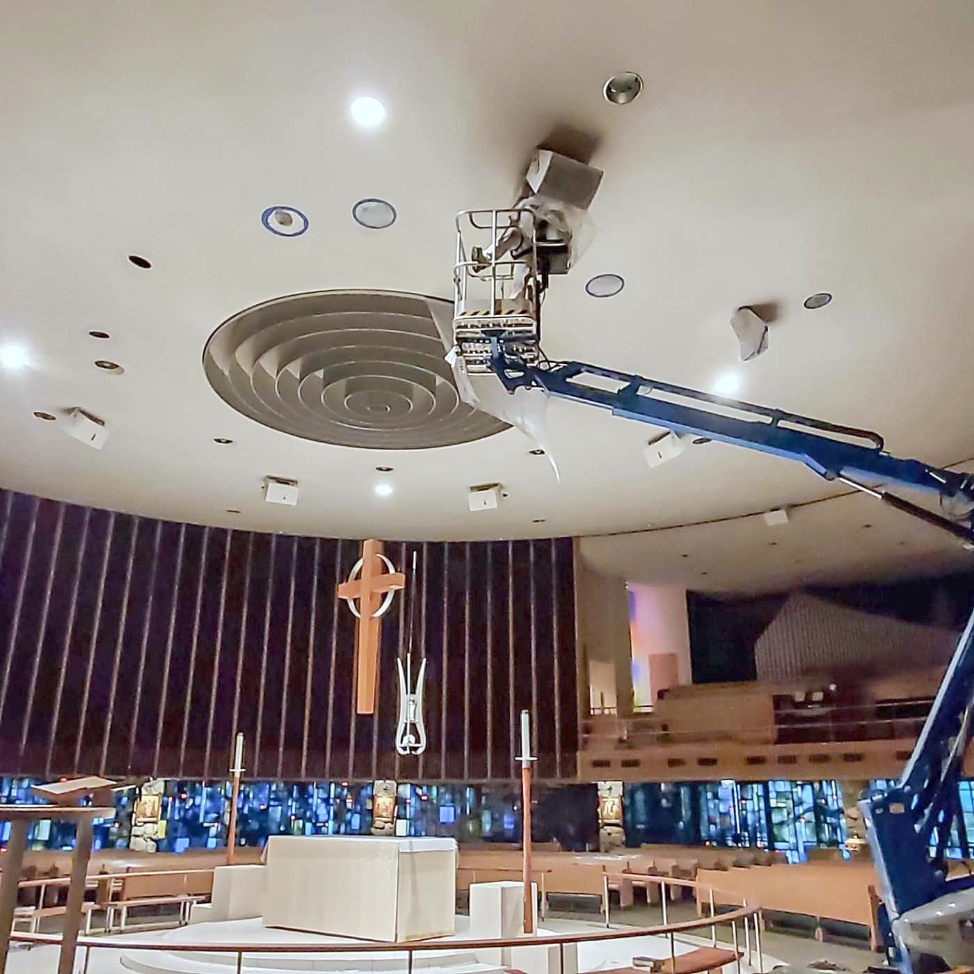 A boom lift raised to the ceiling inside a church sanctuary, with the pews below
