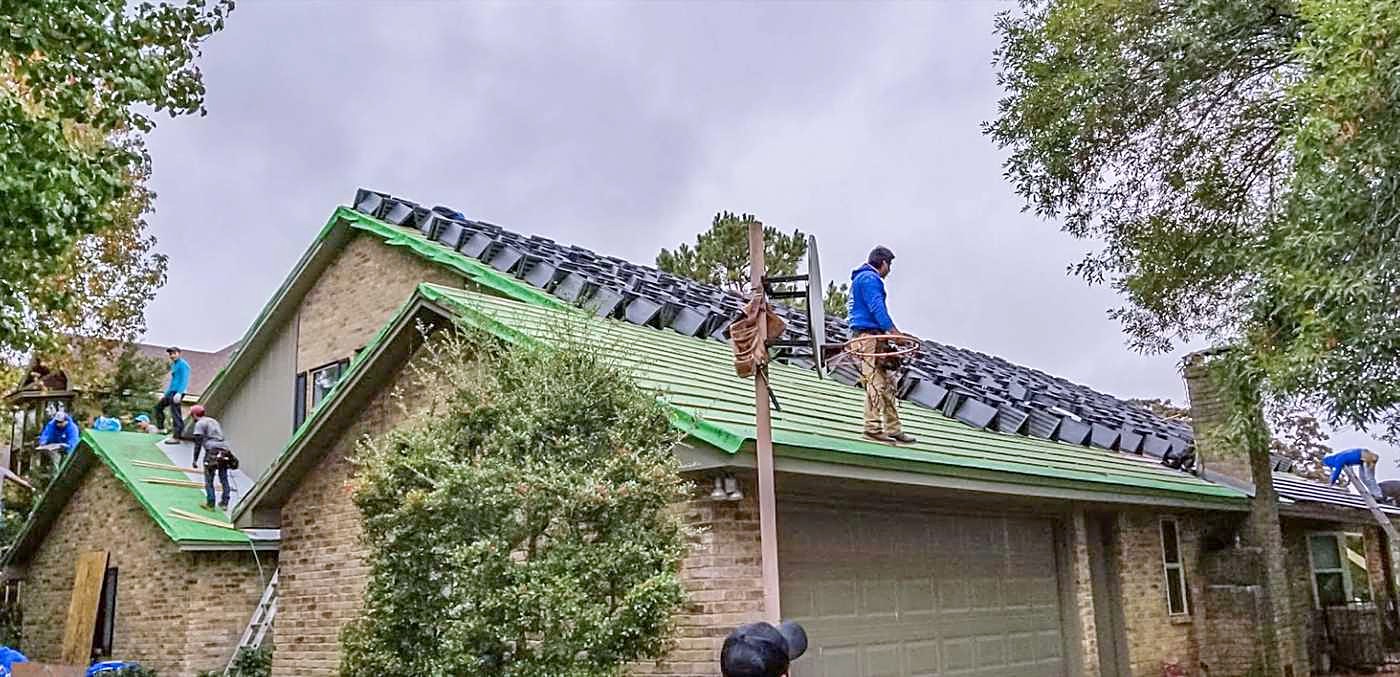 A crew working across a low-slope roof, with material staged along one edge