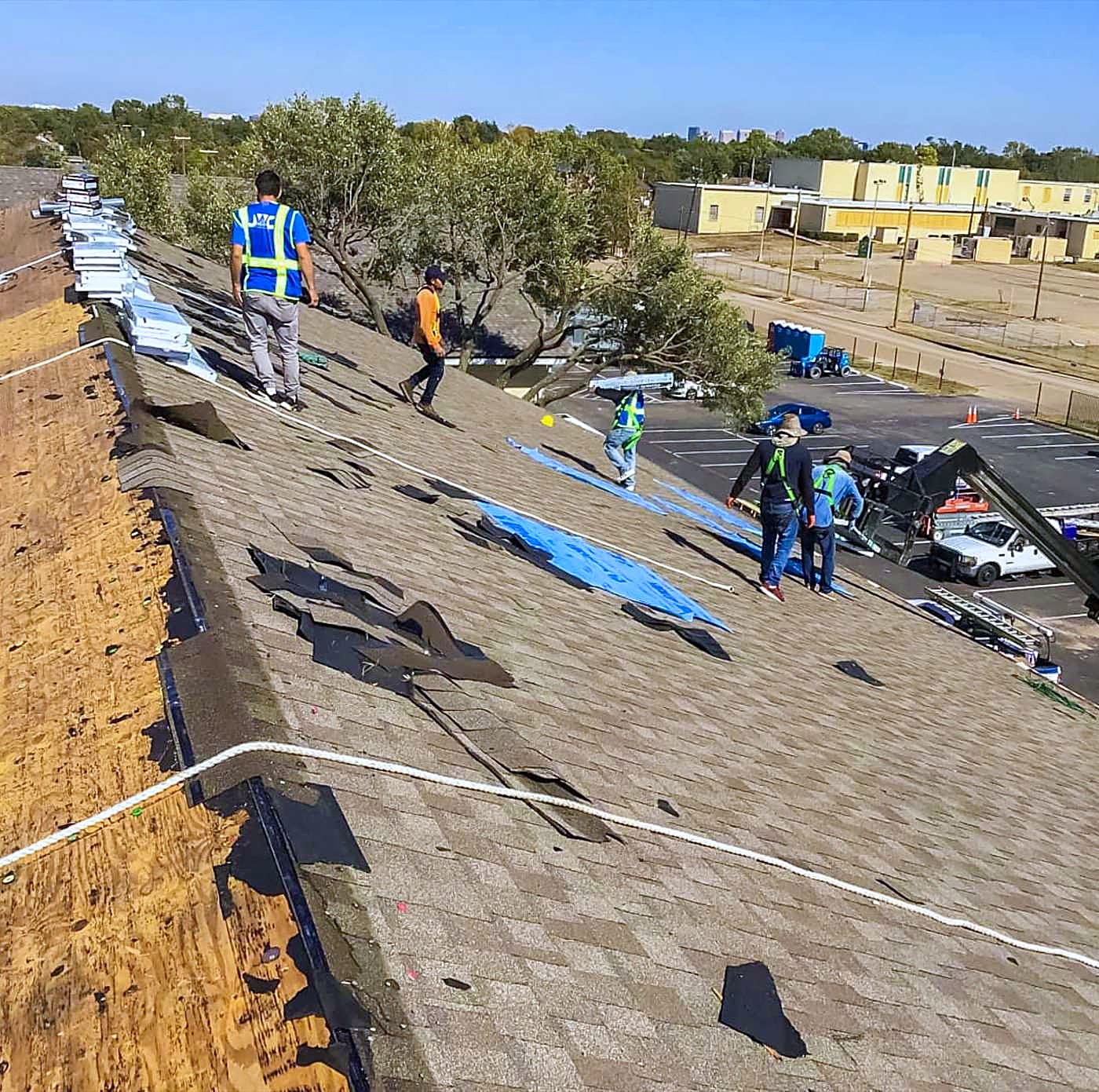 A crew stripping old shingles off a residential roof, with tarps laid out below