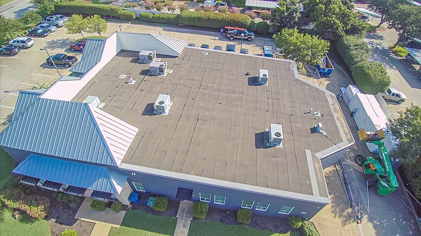 Drone view of a commercial building with a large low-slope roof, rooftop units and a blue standing-seam mansard edge