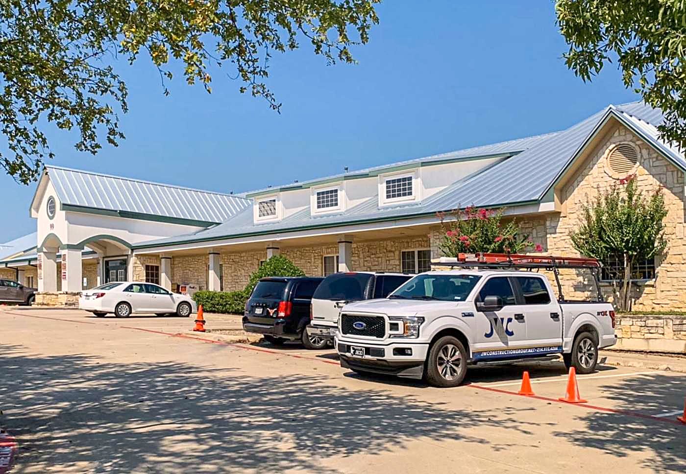 A long standing seam metal roof on a single-story building, with trucks parked along the front