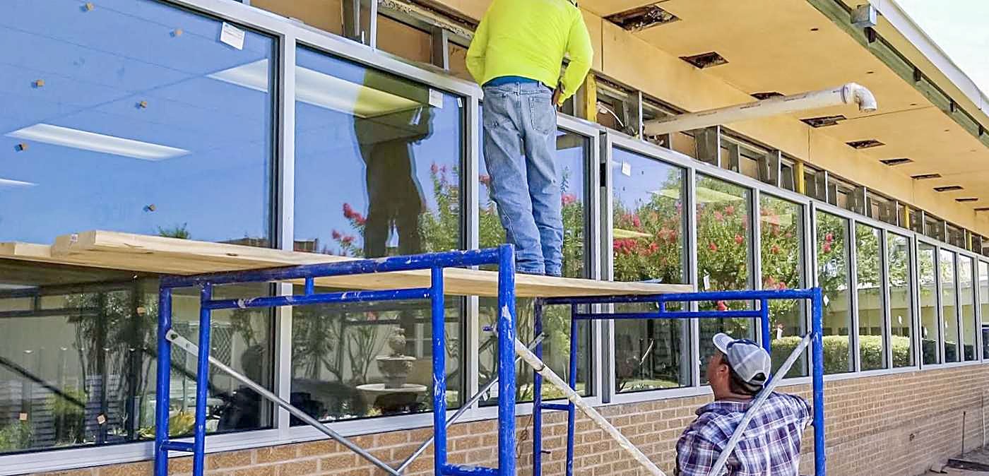 Workers on scaffolding along a commercial storefront glazing run